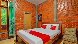A room with a brick wall, a wooden bed with red and white bedding, a green curtain, and a patterned chair. - OYO 90031 Villa Papada (Batu)