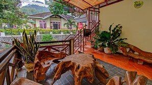 A wooden table and bench set on a tiled floor with a view of a house and greenery in the background. - OYO 90031 Villa Papada (Batu)