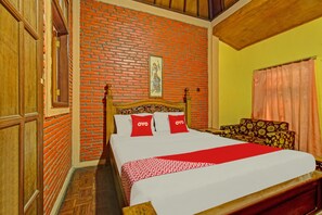 A room with a brick wall, a bed with white bedding and red pillows, a wooden headboard, and a floral-patterned sofa. - OYO 90031 Villa Papada (Batu)