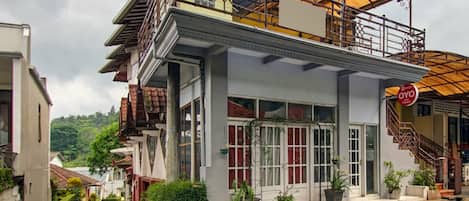 Un edificio de dos pisos con un balcón, ventanas amplias y un letrero que indica un hotel.