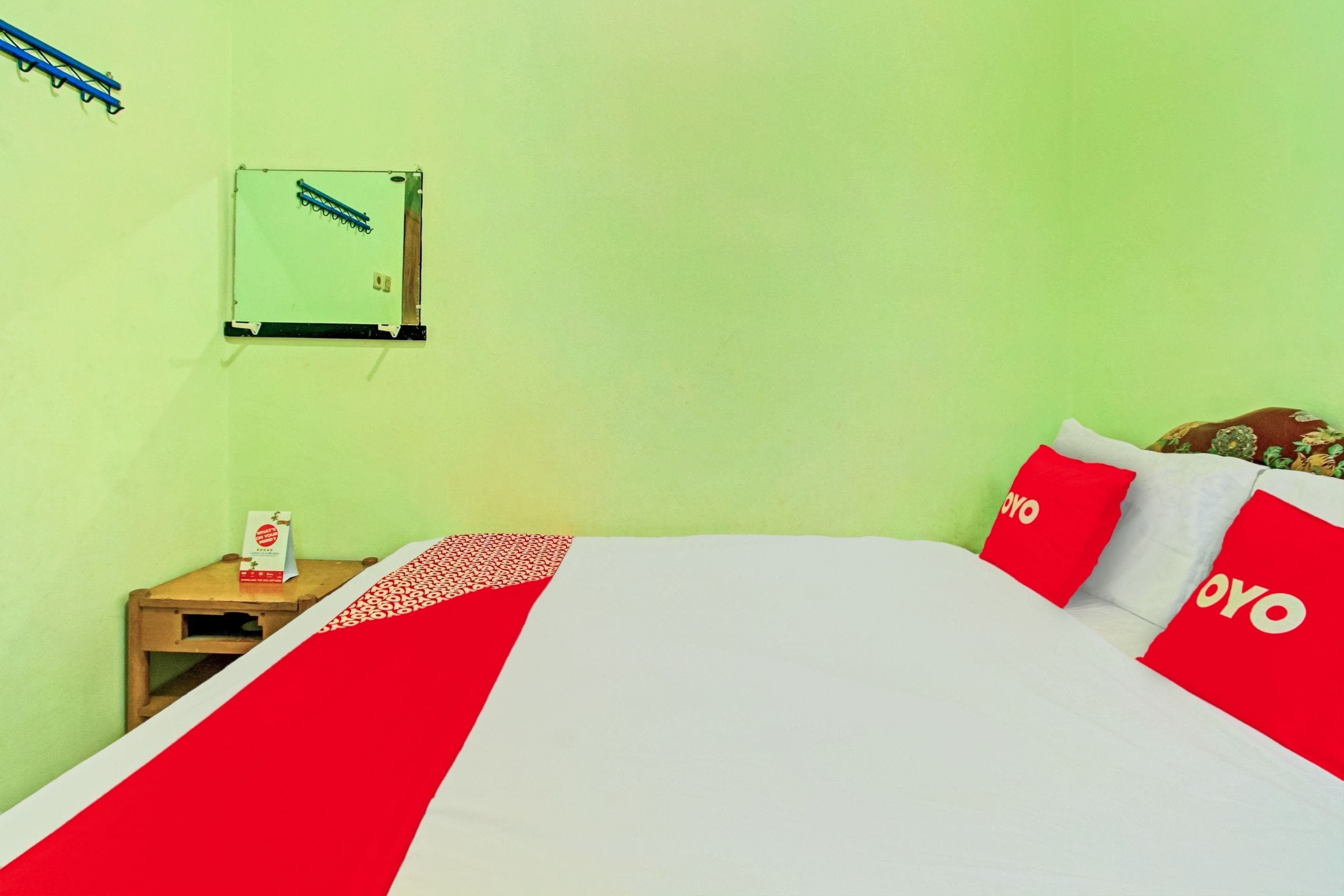 A hotel room with a bed, a nightstand, a wall-mounted air conditioning unit, and a window with a curtain.
