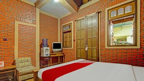 Ein Hotelzimmer mit einer Ziegelwand, einem Bett mit roter Bettdecke, einem Holzschrank, einem Fernseher auf einem Holztisch und einem kleinen Tisch mit Stuhl.