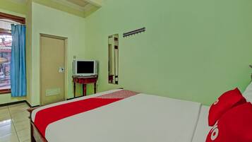 A hotel room with a bed, a television on a stand, a mirror, and a window with curtains.
