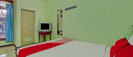 A hotel room with a bed, a television on a stand, a mirror, and a window with curtains.