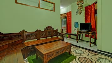 A traditional wooden sofa set with intricate carvings, a matching wooden coffee table, and a television on a stand.