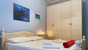 Un dormitorio con cama, mesita de noche, lámpara, armario y dos cuadros colgados en la pared.