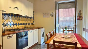 Cocina compacta con estufa a gas, horno y lavadora, una mesa de comedor con sillas y una ventana con persianas.
