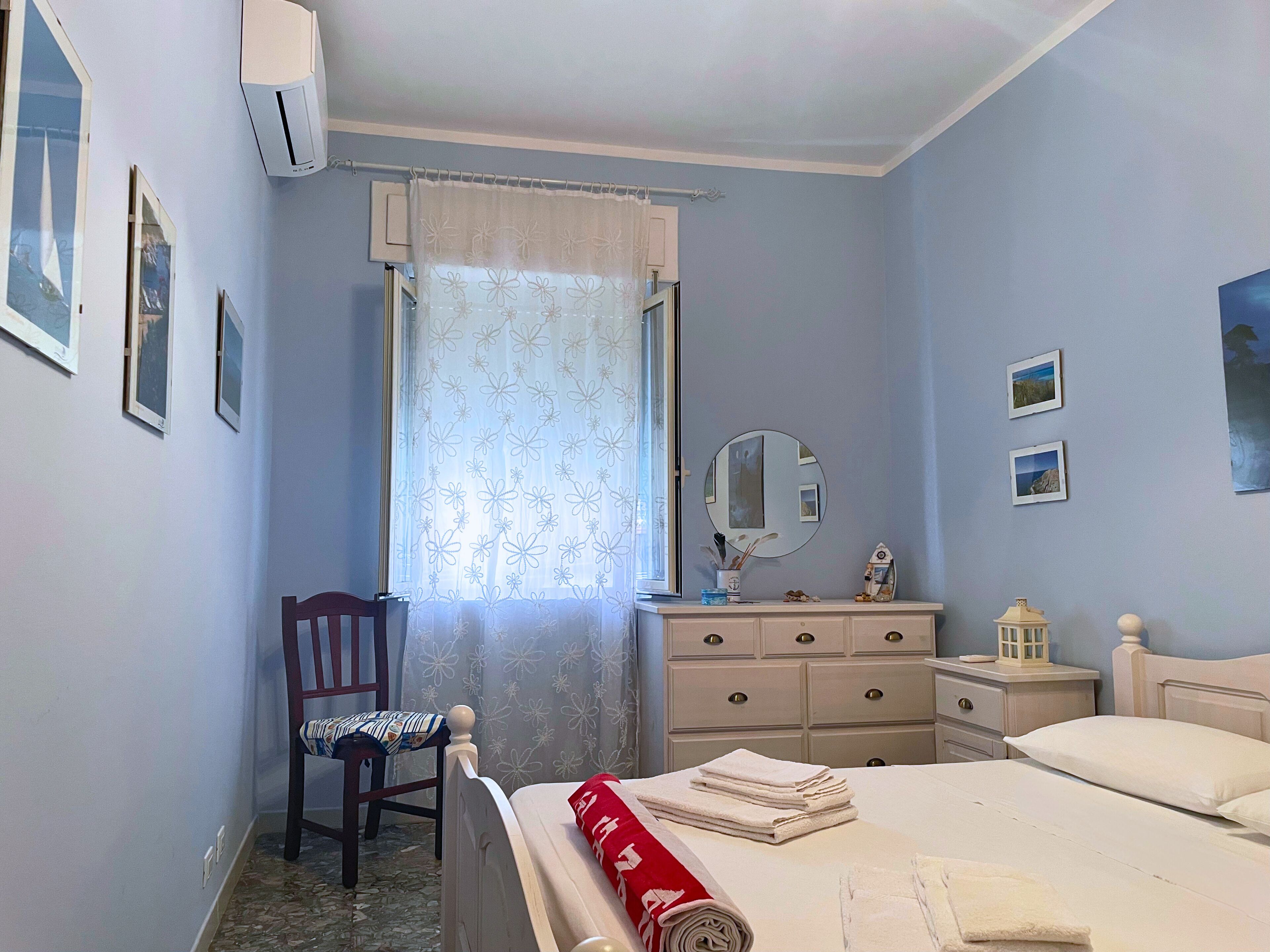 A bedroom with a bed, a dresser, a chair, a mirror, and framed pictures on the wall.