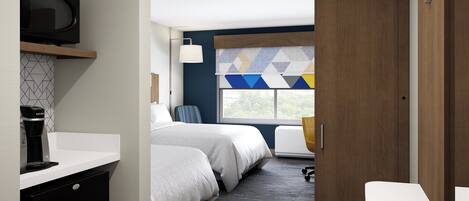 Ein modernes Hotelzimmer mit einem Bett, einem Schreibtisch, einem Sessel, einem Fernseher und einem Fenster mit einem geometrischen Vorhang.