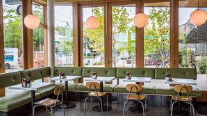 Ein Restaurant mit grünen Sitzbänken und Tischen, großen Fenstern und hängenden Pendelleuchten.