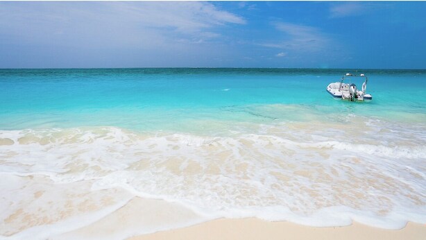 Een strand met helder turquoise water en een boot in de verte.