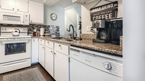 A modern kitchen with white cabinets, a granite countertop, a coffee machine, and a clock on the wall. - Creekside Home | 3 BR/3BA | PVT Hot Tub (Frisco)