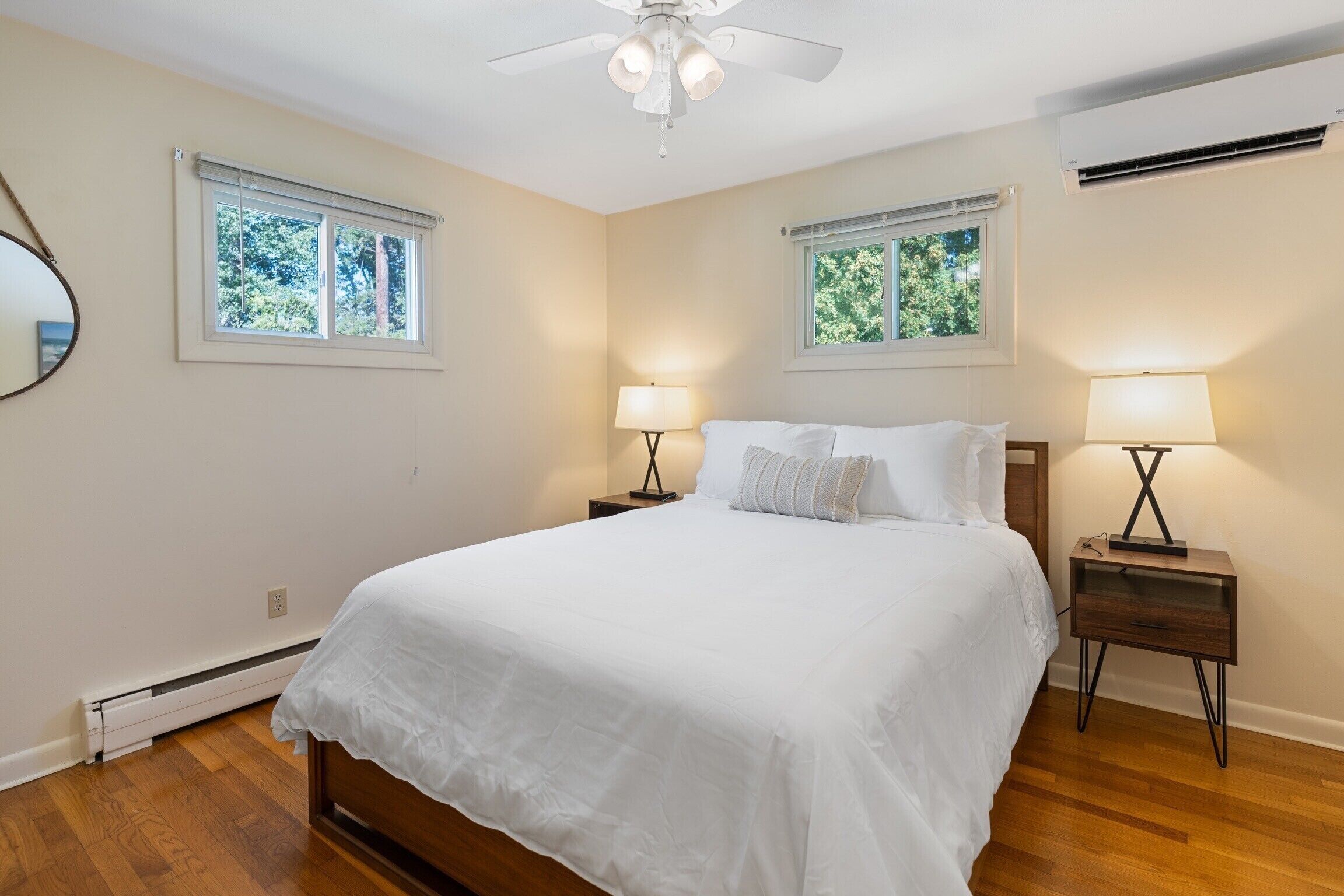 A bedroom with a large bed, two bedside tables with lamps, a ceiling fan, and two windows with blinds.