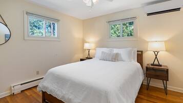 A bedroom with a large bed, two bedside tables with lamps, a ceiling fan, and two windows with blinds.