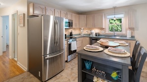 Cozinha moderna com eletrodomésticos de aço inoxidável, armários de madeira e um espaço de jantar com mesa posta para quatro pessoas.