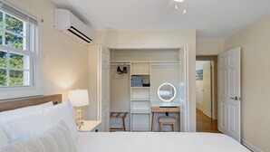 Quarto com cama, mesa de cabeceira, abajur e um closet espaçoso com prateleiras e espelho.