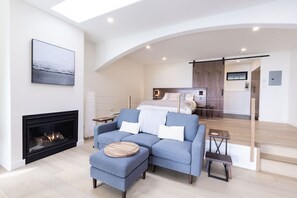 A modern bedroom with a bed, a blue sofa, a fireplace, and a staircase leading to another room.