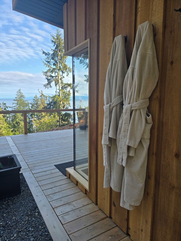 A wooden deck with a glass door leading to a balcony overlooking a forest and a body of water.