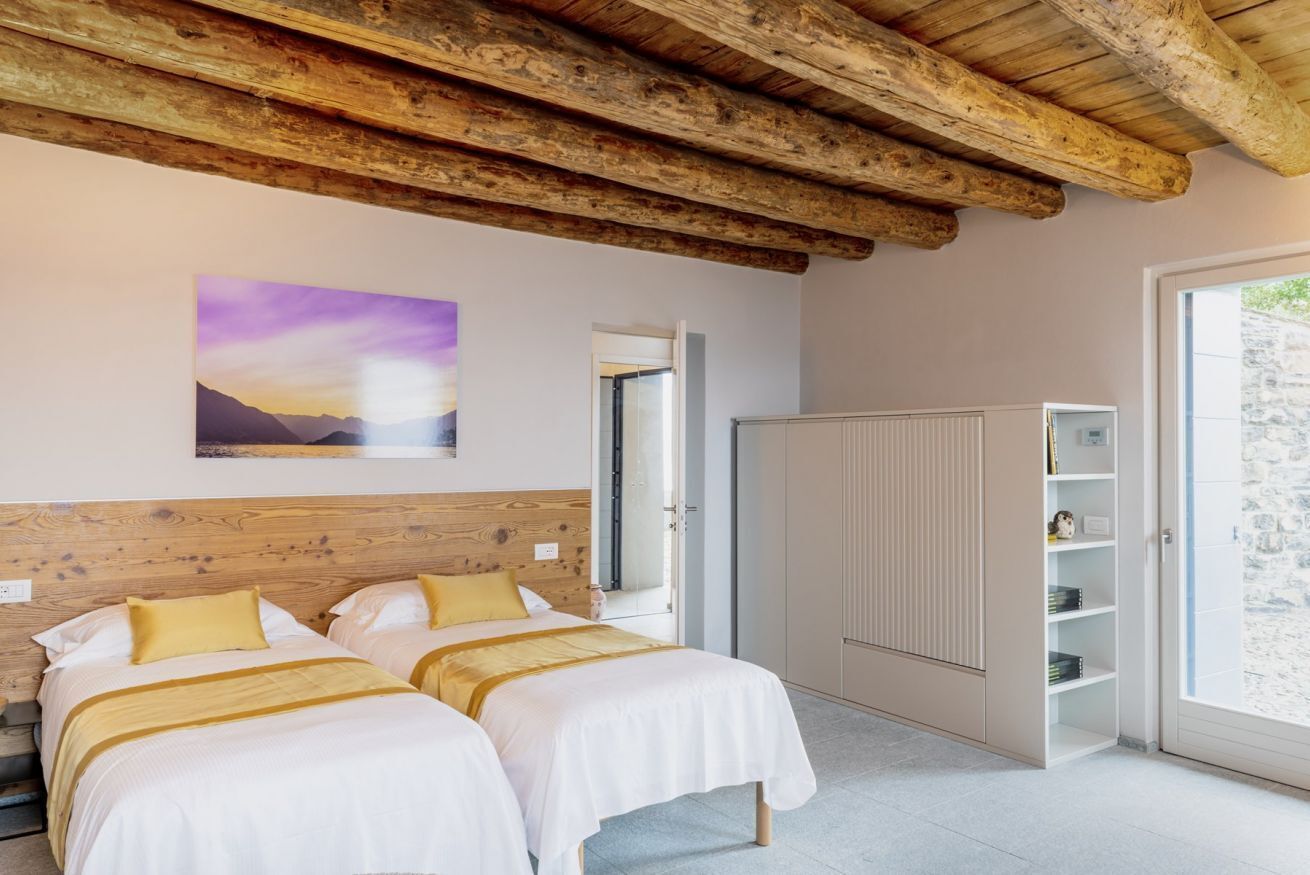 A bedroom with two beds, a wooden ceiling, a painting on the wall, and a wardrobe.