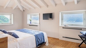 Un dormitorio con cama, dos ventanas, televisor y vista al mar.