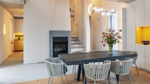 Un comedor moderno con una mesa de madera oscura y sillas blancas, una chimenea y una escalera que sube a un nivel superior.