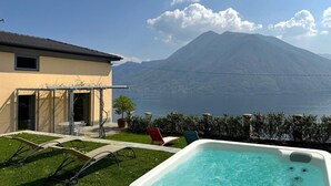 Zona de piscina con sillones, un jacuzzi y vistas a una montaña y un lago.