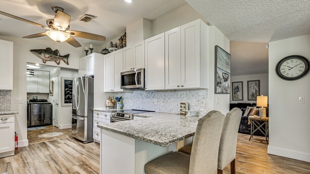 A modern kitchen with white cabinets, a granite countertop, and a bar area with a chair. - Waterfront Home on Canal w/ Dock & Pedal Boat! (Crystal River)