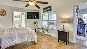 A bedroom with a bed, a ceiling fan, a nightstand, a window with blinds, and a door leading to another room. - Waterfront Home on Canal w/ Dock & Pedal Boat! (Crystal River)