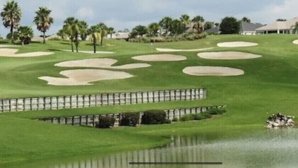 Un campo de golf con búnkeres de arena, una zona de agua y palmeras.
