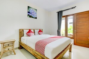 A bedroom with a wooden bed frame, white bedding, red pillows, a red and white patterned throw, a nightstand with drawers, a wooden door, and a window with curtains. - OYO 90232 March 67 Stay (Denpasar)