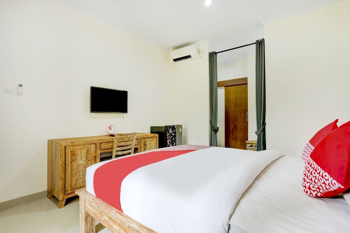 A hotel room with a bed, a wooden dresser, a television, and an air conditioning unit.