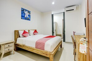 A bedroom with a wooden bed, white bedding, red pillows, a small bedside table, a mirror, an air conditioning unit, and a wooden desk with a sign. - OYO 90232 March 67 Stay (Denpasar)
