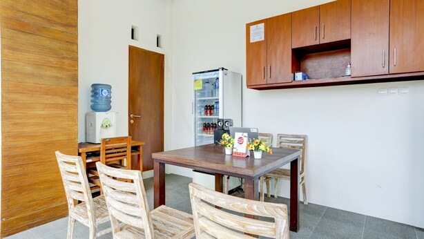 A small kitchen with wooden cabinets, a refrigerator, and a dining table with chairs. - OYO 90232 March 67 Stay (Denpasar)