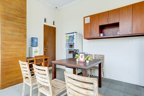 A small kitchen with wooden cabinets, a refrigerator, and a dining table with chairs. - OYO 90232 March 67 Stay (Denpasar)