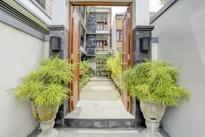 Un étroit sentier mène à un bâtiment à l’architecture moderne, bordé de plantes en pot et doté d’une entrée décorative.