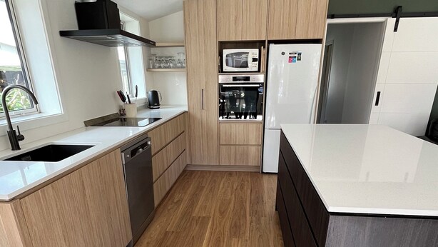 Una cocina moderna con armarios de madera, microondas integrado, horno y lavavajillas.