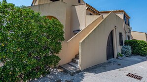 Un edificio de dos pisos con fachada color beige, una pequeña escalera que conduce a la entrada y un cielo azul claro al fondo.