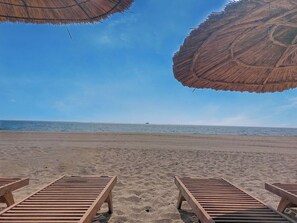 Ein Strand mit Holzliegen und Strohdächern.