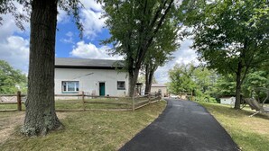 A paved path leading to a white building with a green door, surrounded by trees and a fenced area. - Easy access, roomy, close to so much but in a private country setting. (New Stanton)