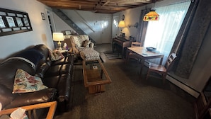 A cozy living room with a leather sofa, patterned armchair, and a wooden coffee table. A staircase leads to a dining area with a table and chairs. - Easy access, roomy, close to so much but in a private country setting. (New Stanton)