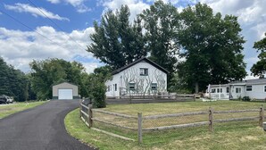 A rural property with a paved driveway leading to a white building with green vines, surrounded by a wooden fence and trees. - Easy access, roomy, close to so much but in a private country setting. (New Stanton)