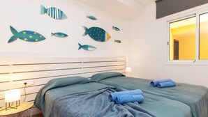 Quarto com cabeceira de madeira, duas camas com roupa de cama combinando, mesa de cabeceira com abajur e parede decorada com arte de peixes.