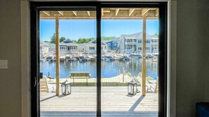 A view through a glass door of a marina with boats, a wooden deck, and buildings in the background. - Kayak Shack: 1st Floor, Waterfront Lake House, Dock Boat & Jet Ski (Sylvan Beach)