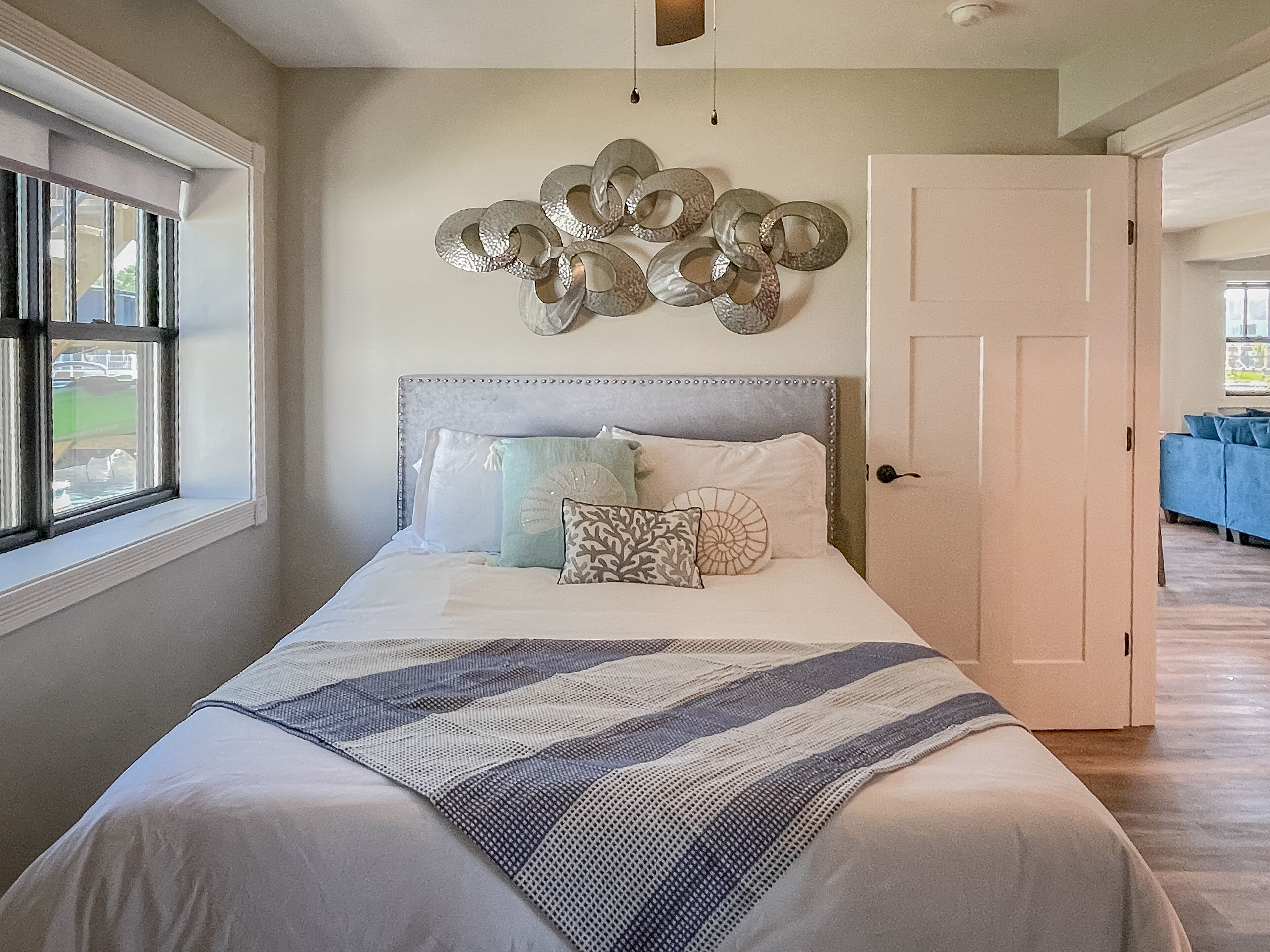 A bedroom with a large bed, a decorative wall piece, and a view of the outdoors through a window.