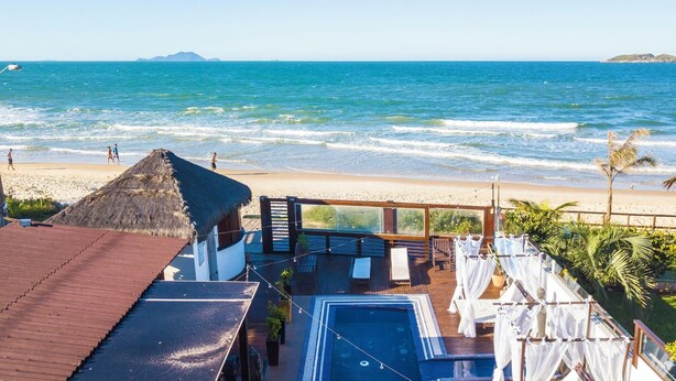 A beachside resort with a pool, a thatched-roof structure, and a view of the ocean.