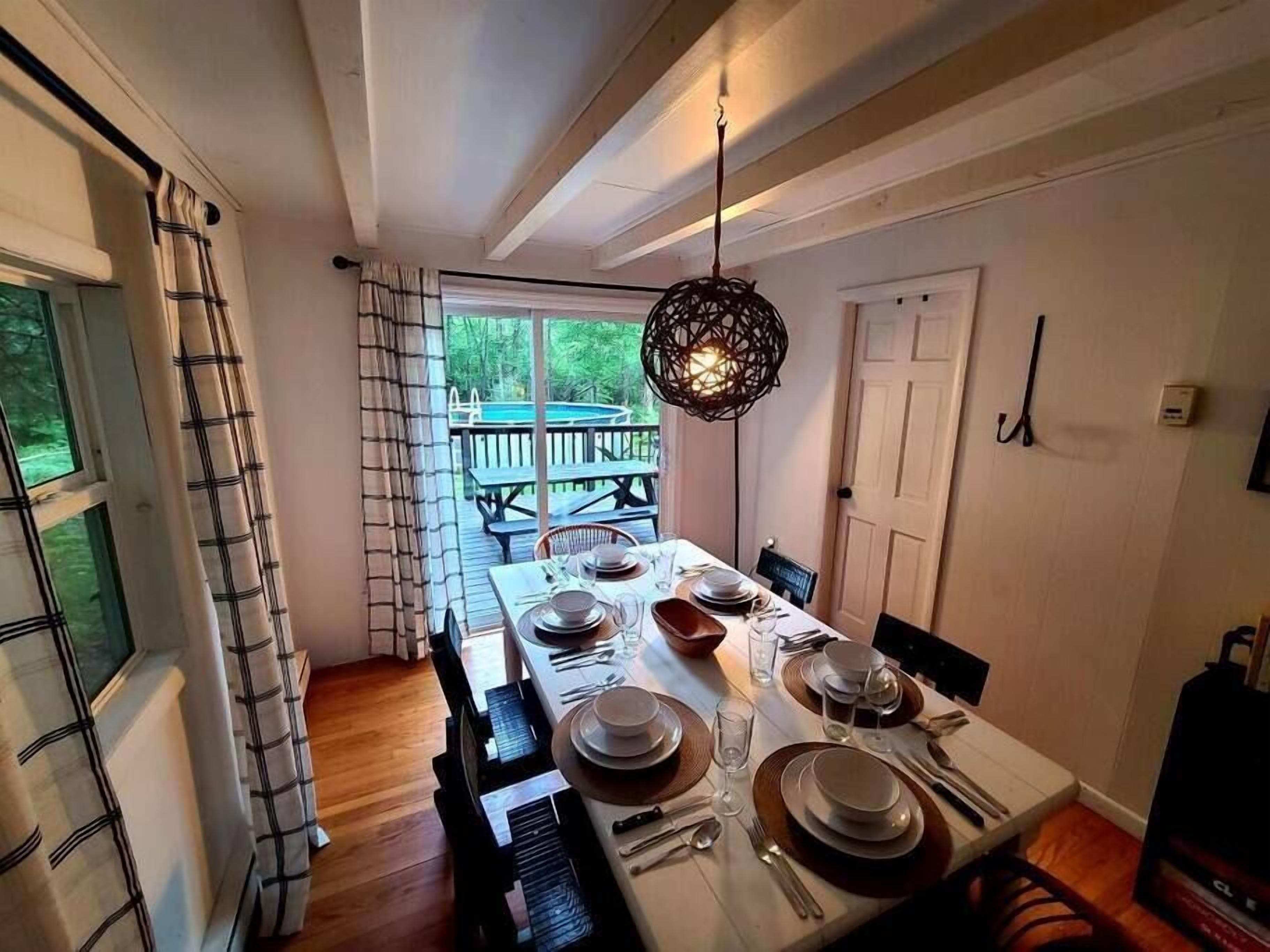 A dining area with a table set for four, a hanging light fixture, and a view of a deck and pool outside.
