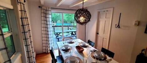 A dining area with a table set for four, a hanging light fixture, and a view of a deck and pool outside.
