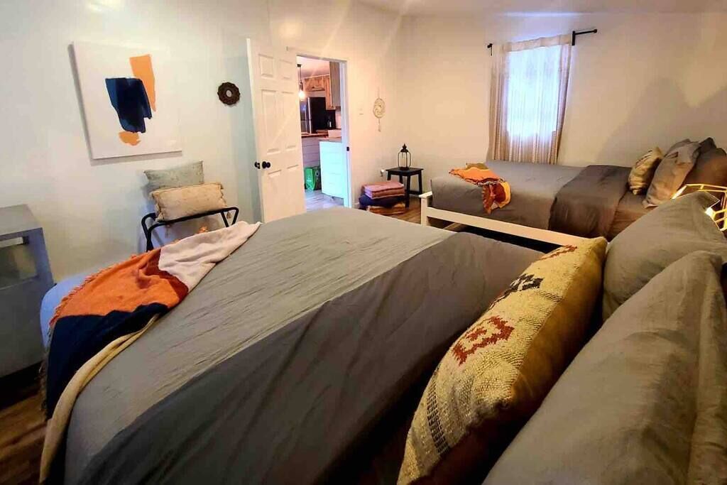 A bedroom with two beds, a bedside table, a lamp, and a door leading to a bathroom.