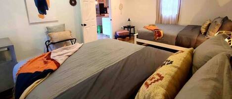 A bedroom with two beds, a bedside table, a lamp, and a door leading to a bathroom.