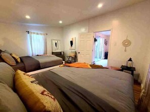 Quarto com duas camas, uma mesa e uma cadeira. Há uma porta que dá para um corredor.